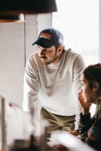 Man and woman engaged in discussion, leaning over desk in modern office setting, warm lighting enhances focus.
